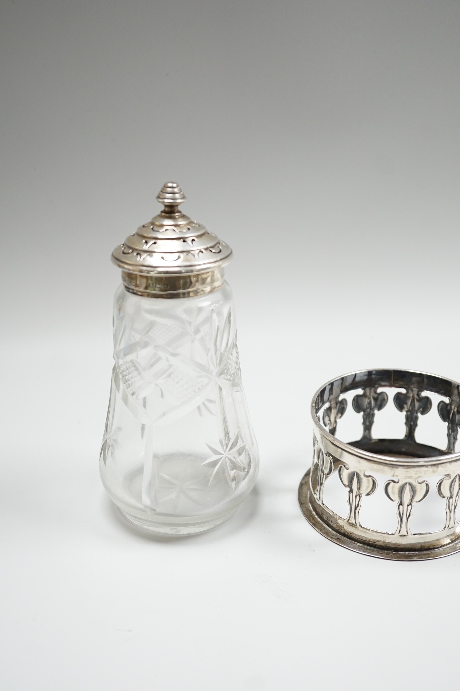 An Edwardian silver bottle? coaster, by William Hutton & Sons, Birmingham, 1902, base diameter 89mm, a pair of George V small silver five bar toastracks and a later silver mounted glass sugar caster.